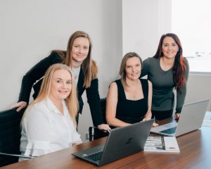 Four women wearing corporate attire smiling at the camera
